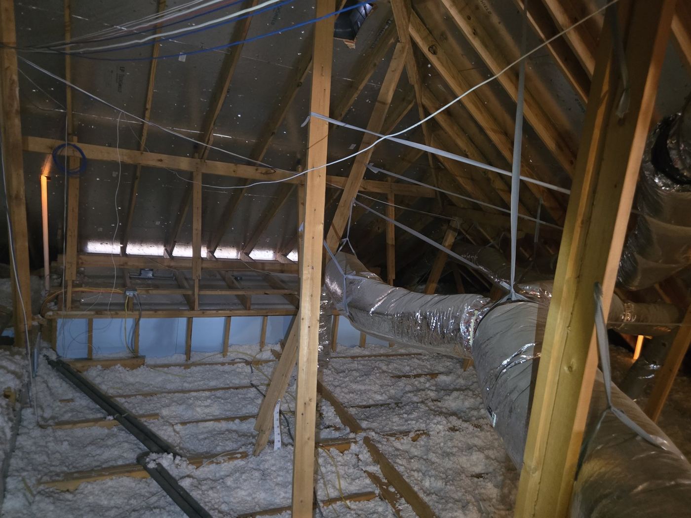Attic with blown-in insulation, flexible HVAC ducts, and wood roof framing during a home inspection