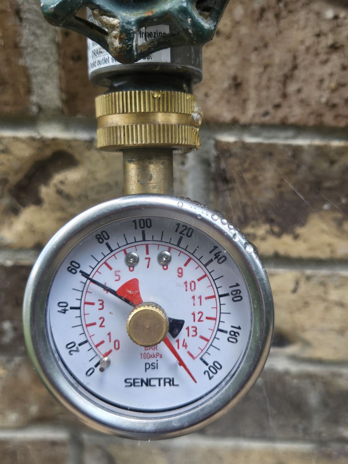 Gas pressure gauge on a brick wall during a home inspection in Conroe, Texas, with water droplets on the gauge glass