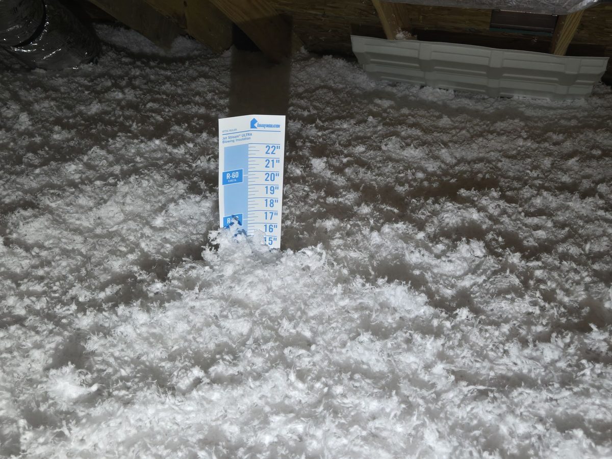 Blown-in attic insulation with a depth ruler standing in it during a Humble, Texas home inspection