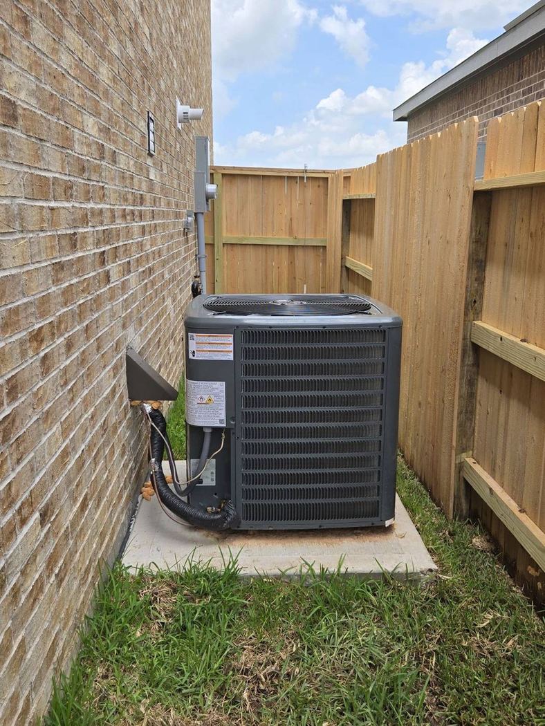 Outdoor air-conditioner condenser on a concrete pad beside a brick wall and wood fence in the Katy, Texas area