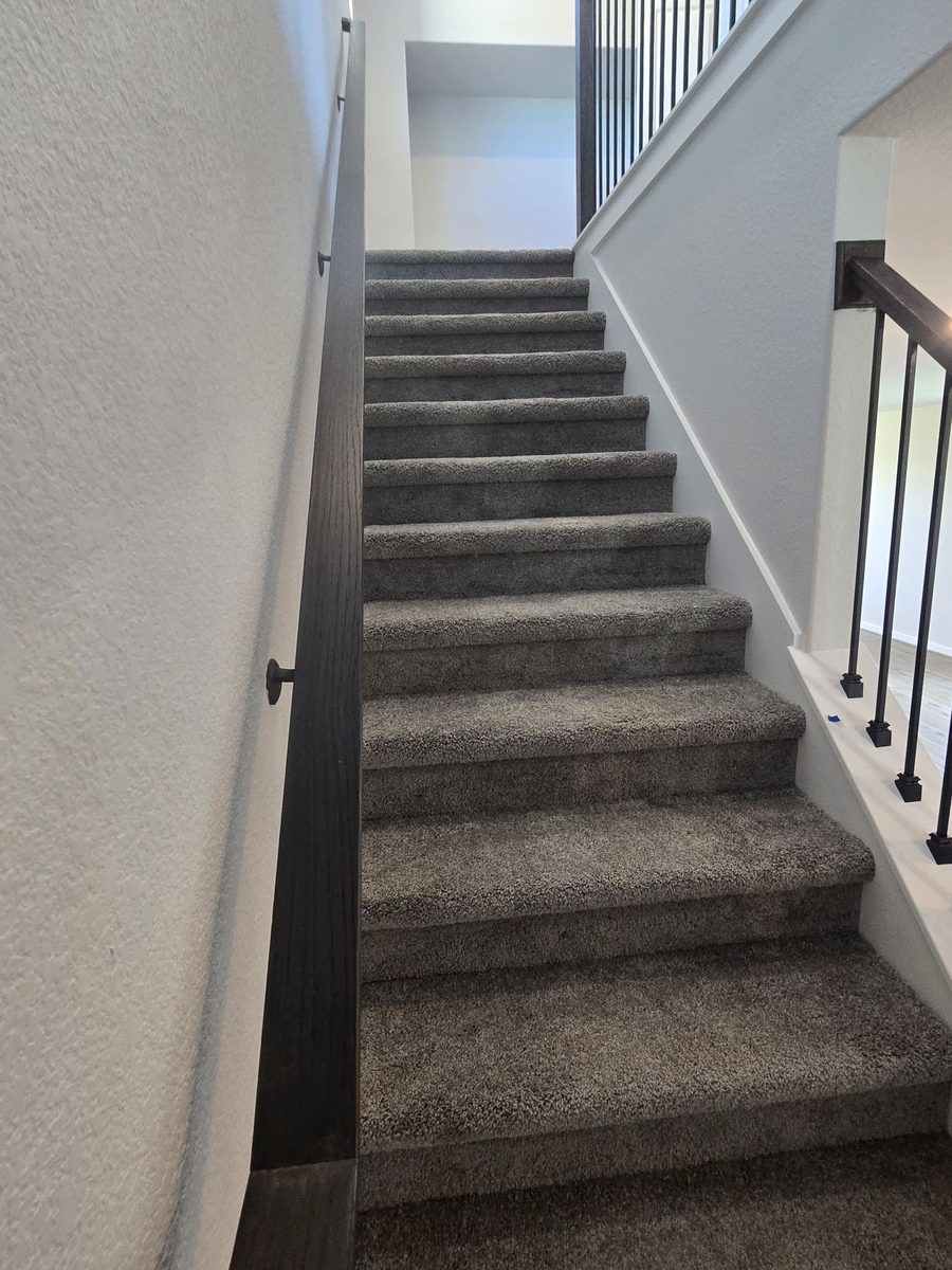 Carpeted stairway with a dark wood handrail and black metal balusters in a Magnolia, Texas home