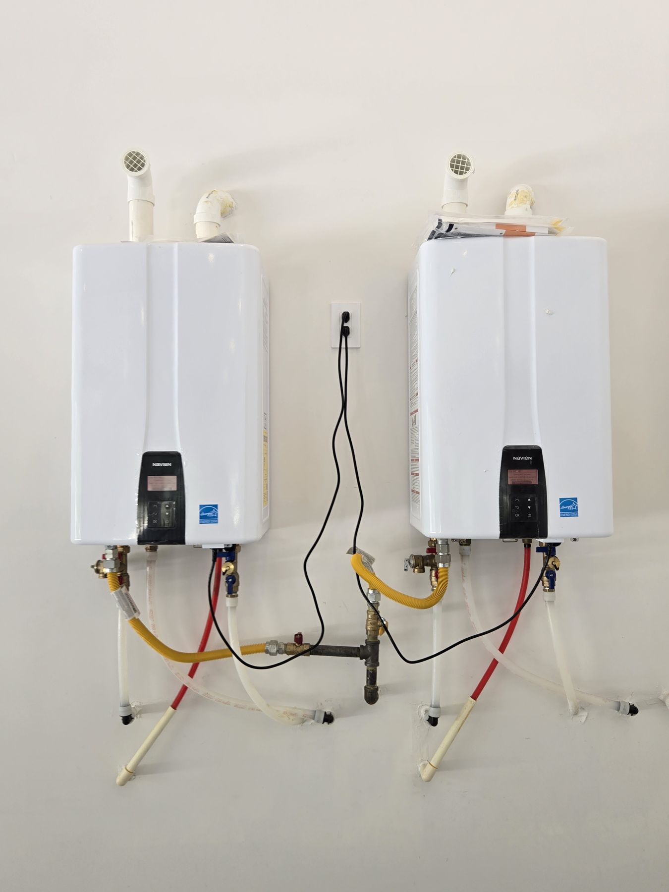 Two wall-mounted tankless water heaters with gas, water, and vent lines in a Montgomery, Texas area home