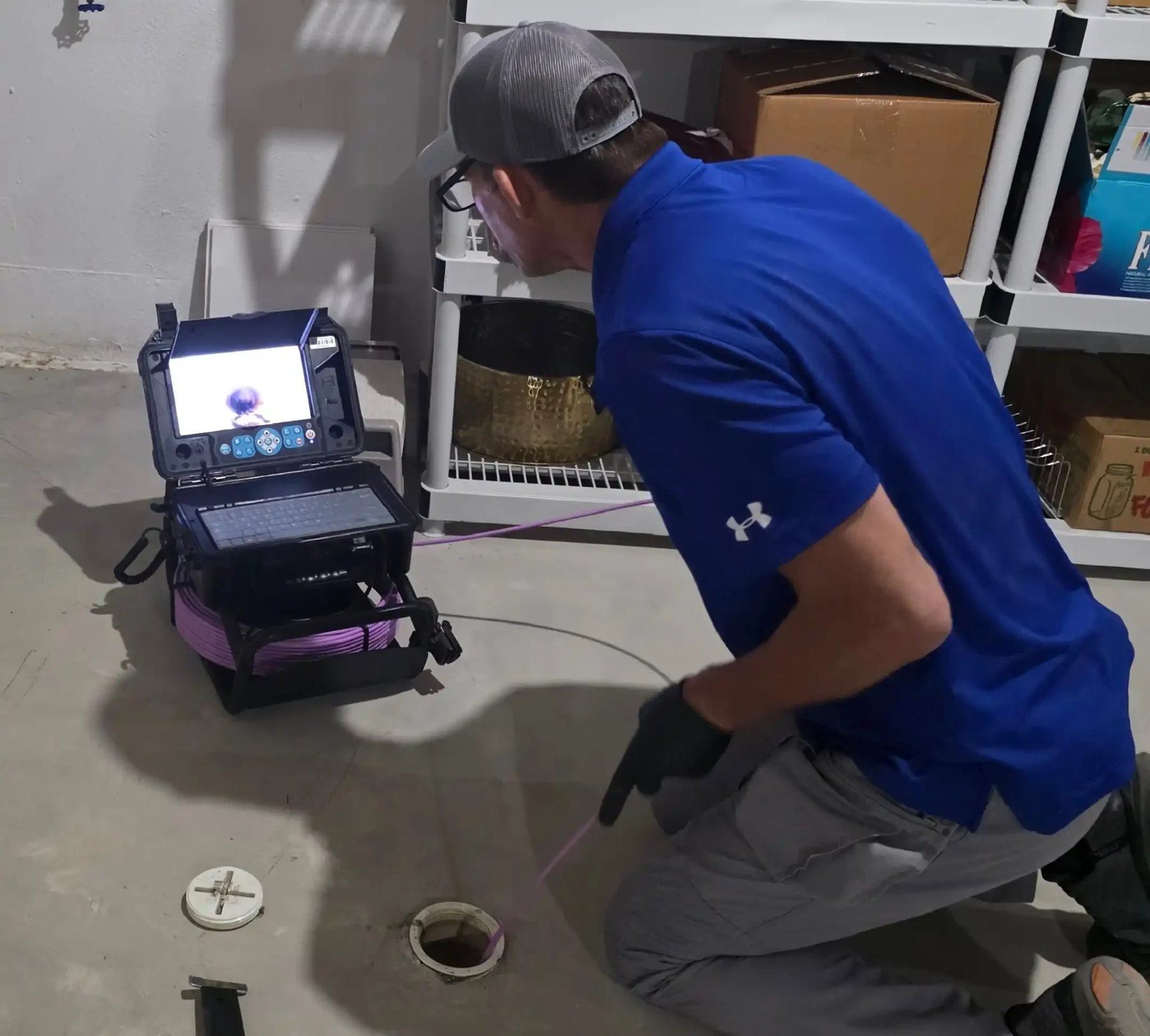 Inspector feeding a sewer camera line into a floor cleanout while watching the monitor