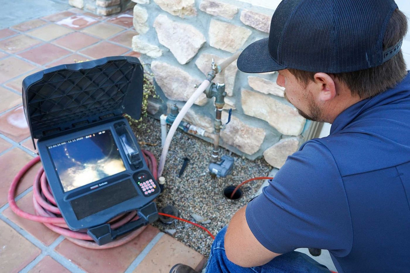 Inspector running a sewer camera from an outdoor cleanout while watching the pipe on a monitor
