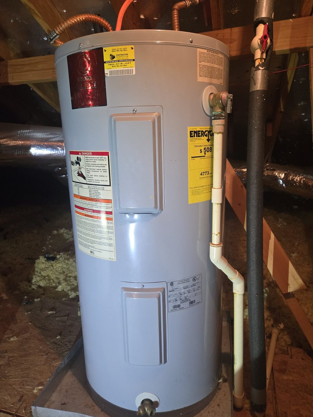 Water heater in an attic with insulated piping and a yellow energy label